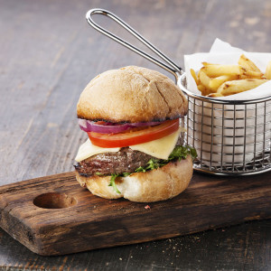 Burger with meat and French fries in basket on wooden background