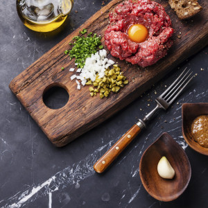 Beef tartare with pickled cucumber and fresh onions on dark marble background