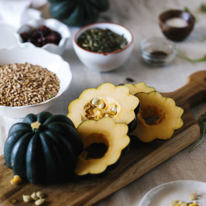 An acorn squash is sliced on a cutting board and displayed with the other ingredients for a roasted acorn squash salad.