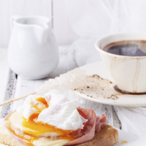 Breakfast with cup of coffee and toast with cheese and poached egg served on white wooden table