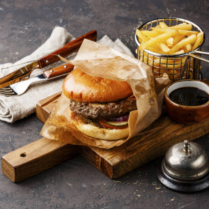 Burger with meat and French fries in basket on dark background and desk bell