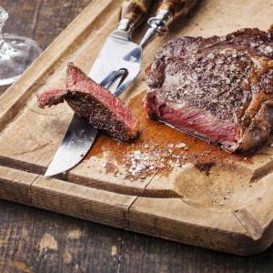 Steak Ribeye with knife and fork for meat on cutting board on dark wooden background
